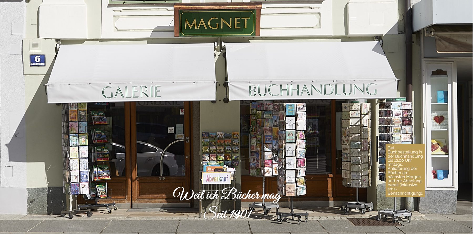 Schaufront der Buchhandlung Magnet am Hauptplatz 6 in Völkermarkt — die Markisen tragen die Aufschriften GALERIE und BUCHHANDLUNG, darüber das gerahmte grün-goldene MAGNET-Schild.